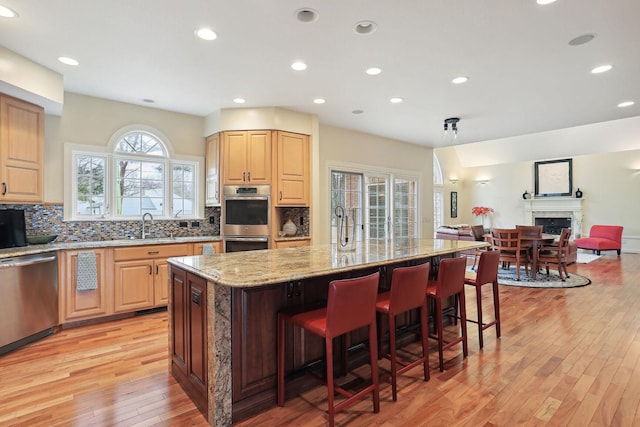 kitchen with appliances with stainless steel finishes, a kitchen breakfast bar, decorative backsplash, light stone countertops, and a center island with sink