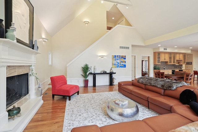 living room with a high end fireplace, high vaulted ceiling, and light hardwood / wood-style flooring