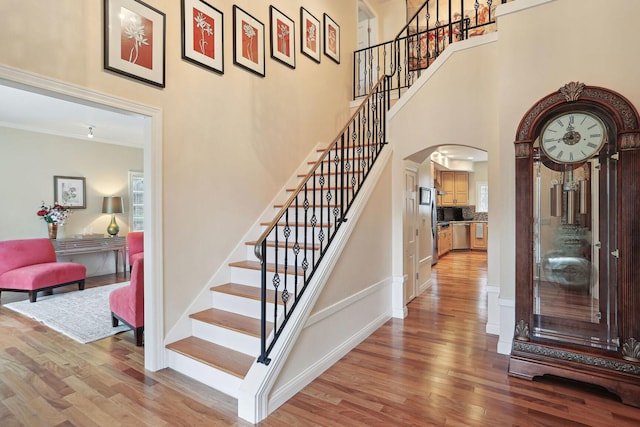 stairway with ornamental molding, a towering ceiling, and hardwood / wood-style floors