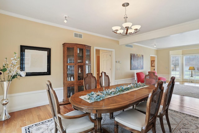 dining area featuring wood-type flooring, ornamental molding, and an inviting chandelier