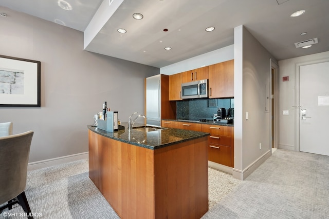 kitchen with black electric cooktop, tasteful backsplash, a kitchen island with sink, dark stone countertops, and sink