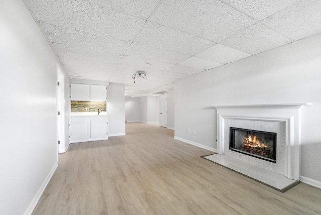 unfurnished living room with light wood-type flooring, a drop ceiling, and sink