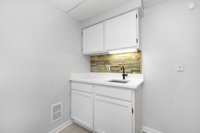 interior space with backsplash, a drop ceiling, white cabinetry, and sink