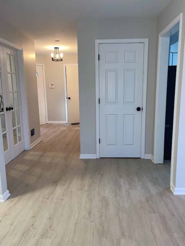 corridor with a chandelier, french doors, and light hardwood / wood-style flooring