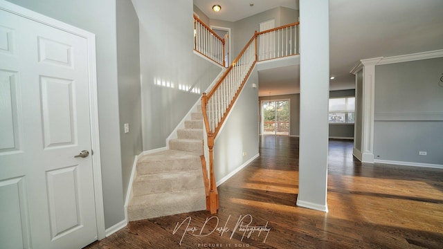 stairs with ornate columns, wood-type flooring, and a towering ceiling