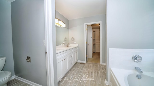 bathroom with vanity, tiled bath, and toilet