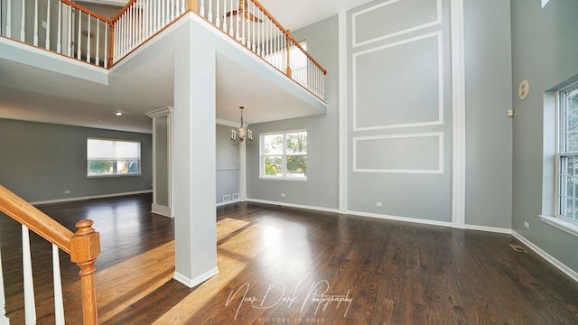 unfurnished living room featuring an inviting chandelier, dark hardwood / wood-style flooring, a wealth of natural light, and a high ceiling