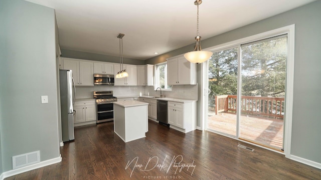 kitchen with a kitchen island, appliances with stainless steel finishes, white cabinetry, sink, and hanging light fixtures