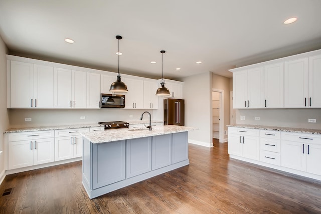 kitchen featuring dark wood-type flooring, white cabinets, pendant lighting, high end appliances, and a kitchen island with sink