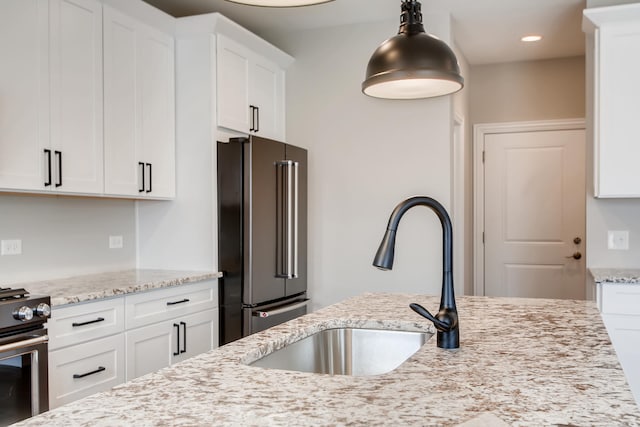 kitchen with pendant lighting, stainless steel appliances, white cabinetry, light stone counters, and sink