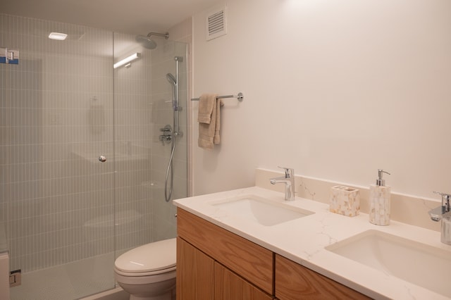 bathroom with toilet, tiled shower, and double vanity