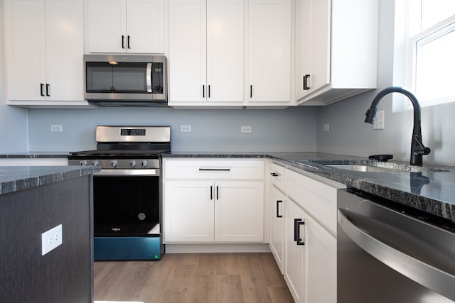 kitchen with white cabinetry, appliances with stainless steel finishes, sink, light wood-type flooring, and dark stone counters