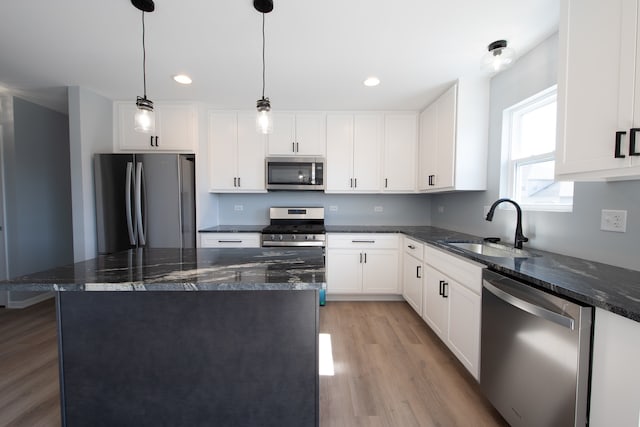 kitchen with appliances with stainless steel finishes, hanging light fixtures, dark stone counters, sink, and light hardwood / wood-style flooring