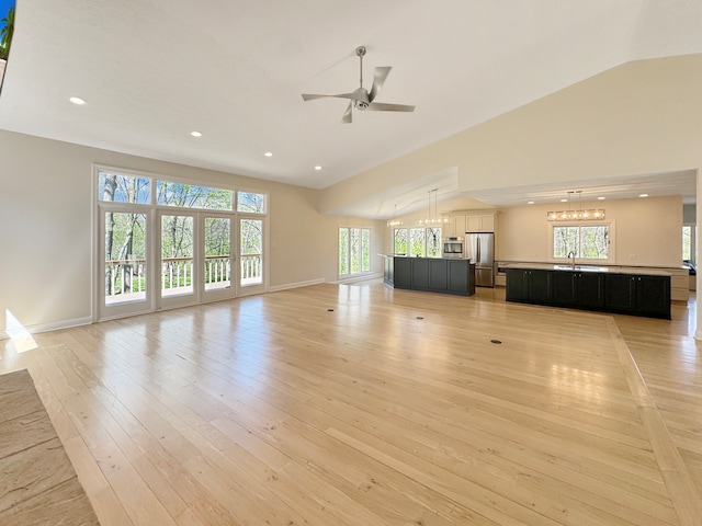 unfurnished living room with sink, light hardwood / wood-style flooring, lofted ceiling, and ceiling fan with notable chandelier