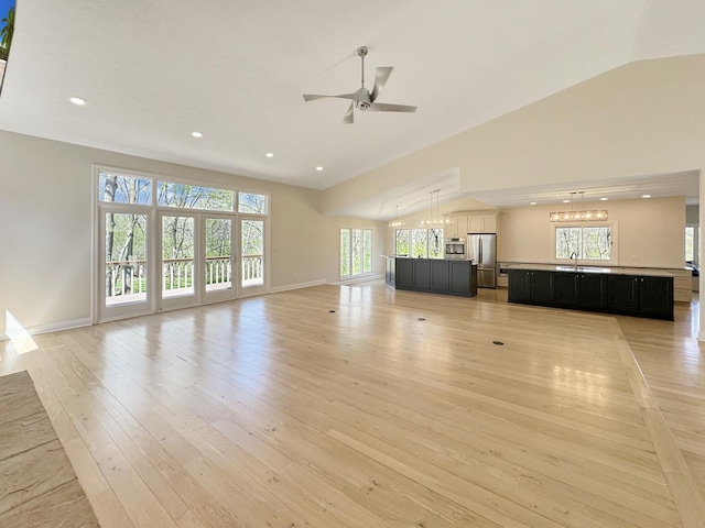 unfurnished living room with lofted ceiling, plenty of natural light, ceiling fan with notable chandelier, and light hardwood / wood-style flooring