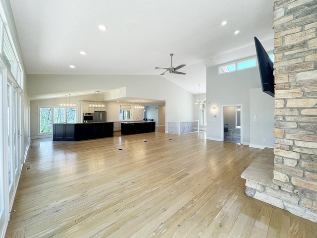 unfurnished living room featuring ceiling fan with notable chandelier, high vaulted ceiling, and light hardwood / wood-style floors