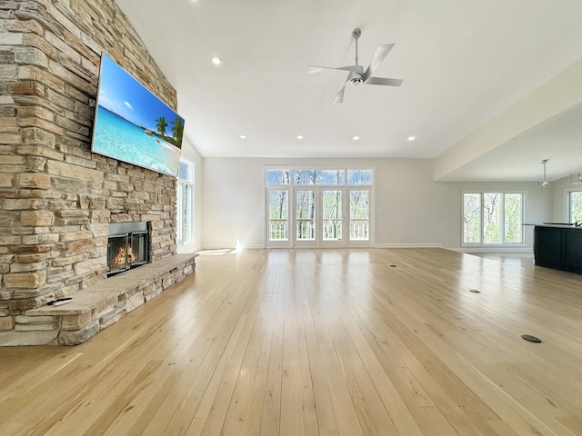 unfurnished living room with ceiling fan, a stone fireplace, and light wood-type flooring