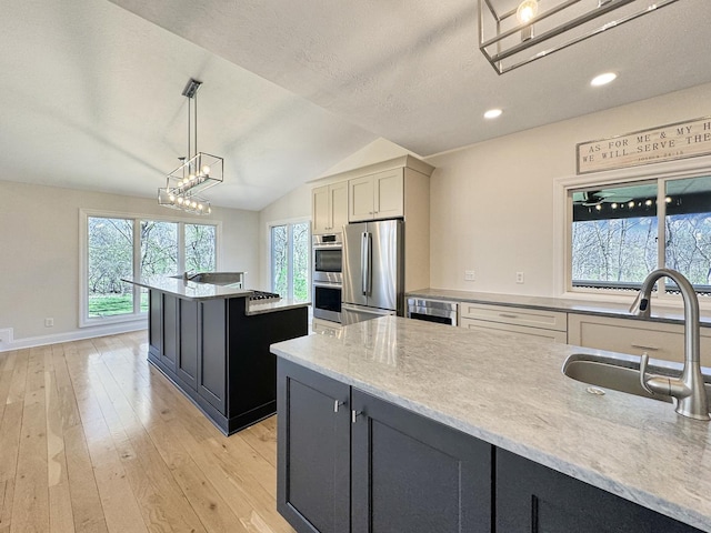 kitchen with pendant lighting, sink, stainless steel appliances, a kitchen island, and light wood-type flooring