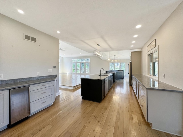 kitchen featuring pendant lighting, stainless steel refrigerator, refrigerator, a center island with sink, and light wood-type flooring