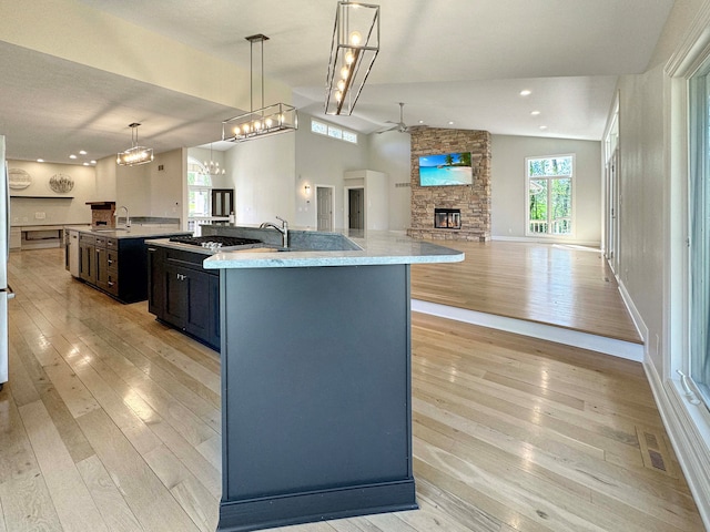 kitchen featuring light hardwood / wood-style floors, sink, a fireplace, decorative light fixtures, and a center island with sink