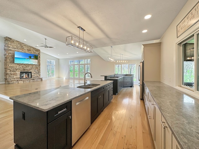 kitchen featuring light wood-type flooring, a large island with sink, a stone fireplace, sink, and lofted ceiling