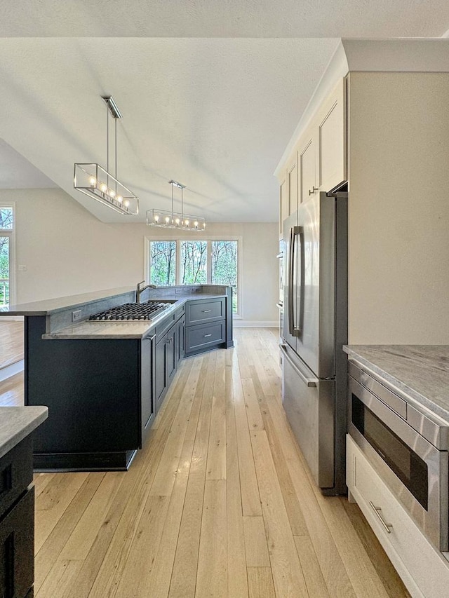 kitchen featuring appliances with stainless steel finishes, white cabinetry, hanging light fixtures, light hardwood / wood-style floors, and a healthy amount of sunlight