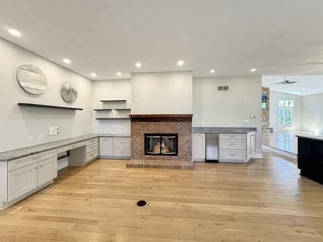 kitchen with ceiling fan, a brick fireplace, built in desk, and light hardwood / wood-style floors