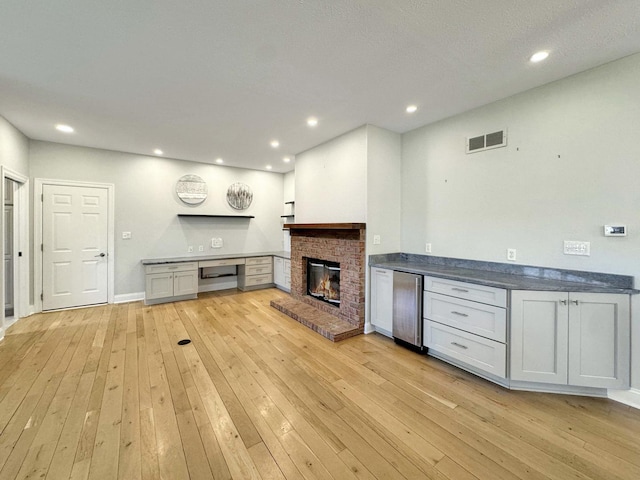 interior space with fridge, built in desk, a fireplace, and light hardwood / wood-style flooring