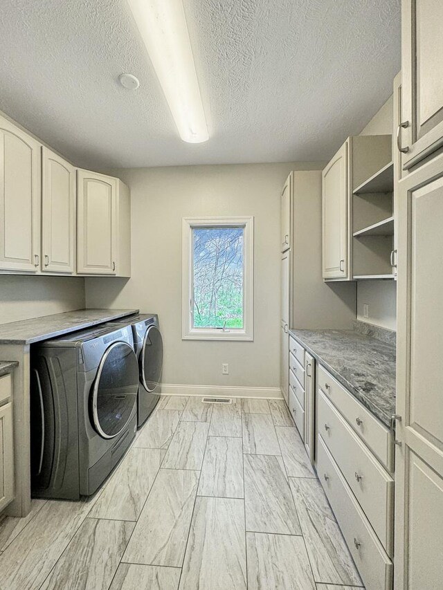 washroom featuring washing machine and dryer, a textured ceiling, cabinets, and light tile patterned floors