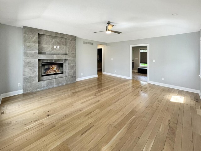 unfurnished living room with a fireplace, light wood-type flooring, vaulted ceiling, tile walls, and ceiling fan