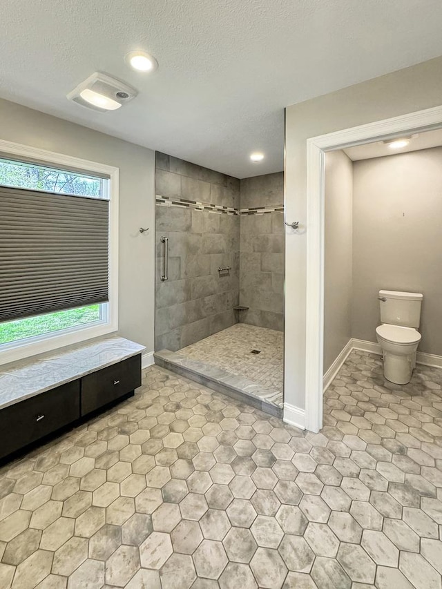 bathroom with a textured ceiling, tile patterned floors, toilet, and tiled shower