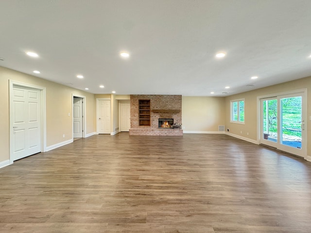 unfurnished living room with light hardwood / wood-style flooring, brick wall, and a brick fireplace