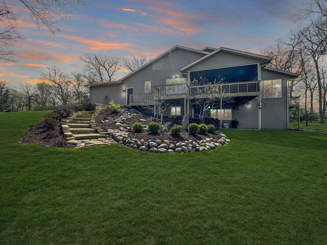 back house at dusk featuring a lawn and a deck