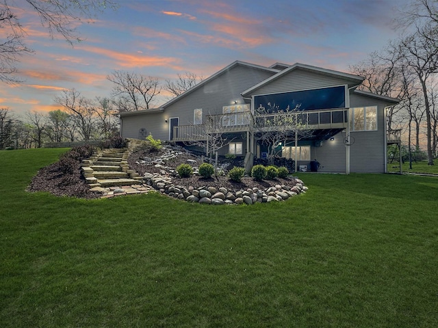 back house at dusk with a wooden deck, a sunroom, and a yard