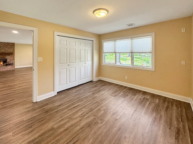 unfurnished bedroom with brick wall, a textured ceiling, wood-type flooring, a closet, and a brick fireplace