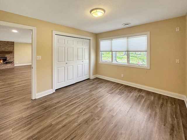 unfurnished bedroom with a brick fireplace, wood-type flooring, and a closet