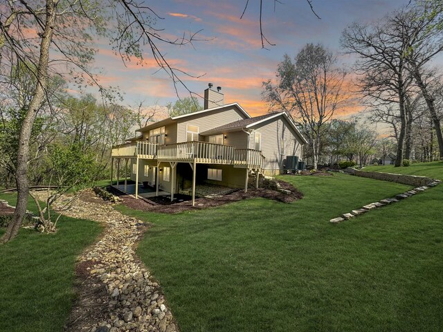 back house at dusk featuring a deck and a lawn