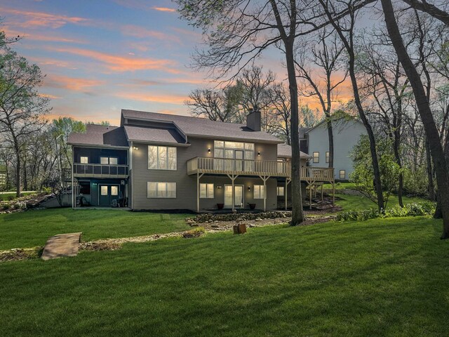 back house at dusk featuring a deck and a lawn