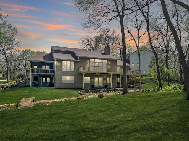 back house at dusk featuring a wooden deck and a yard