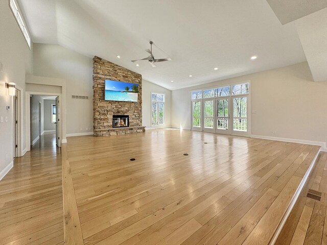 unfurnished living room featuring ceiling fan, high vaulted ceiling, light hardwood / wood-style floors, and a stone fireplace