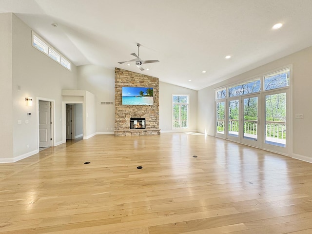 unfurnished living room featuring ceiling fan, high vaulted ceiling, a stone fireplace, and light hardwood / wood-style floors