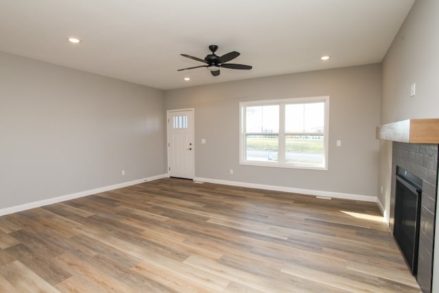 unfurnished living room with a tile fireplace, light hardwood / wood-style floors, and ceiling fan