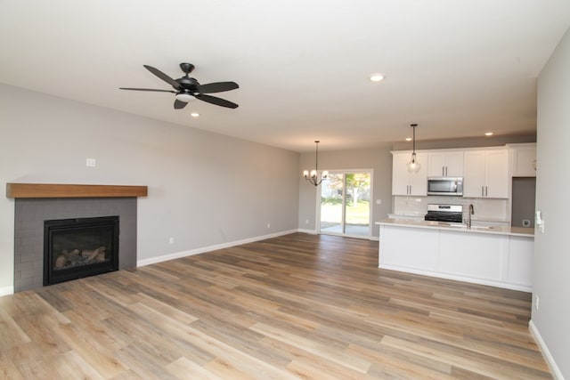 unfurnished living room with a brick fireplace, ceiling fan with notable chandelier, sink, and light wood-type flooring