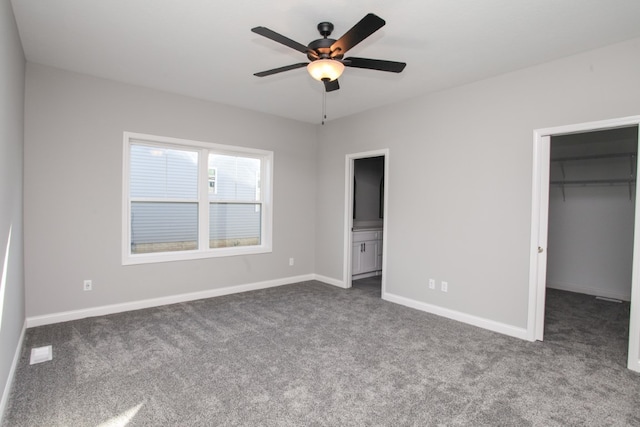 unfurnished bedroom featuring dark colored carpet, ceiling fan, a closet, ensuite bath, and a spacious closet