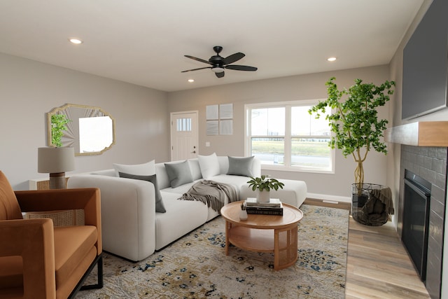 living room featuring a tile fireplace, light hardwood / wood-style floors, and ceiling fan