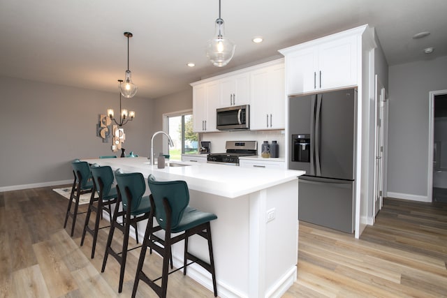 kitchen with a kitchen bar, appliances with stainless steel finishes, a kitchen island with sink, light wood-type flooring, and sink