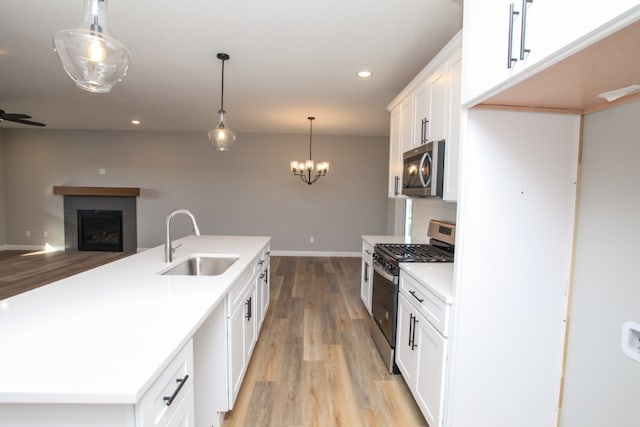 kitchen with appliances with stainless steel finishes, pendant lighting, light wood-type flooring, sink, and white cabinets