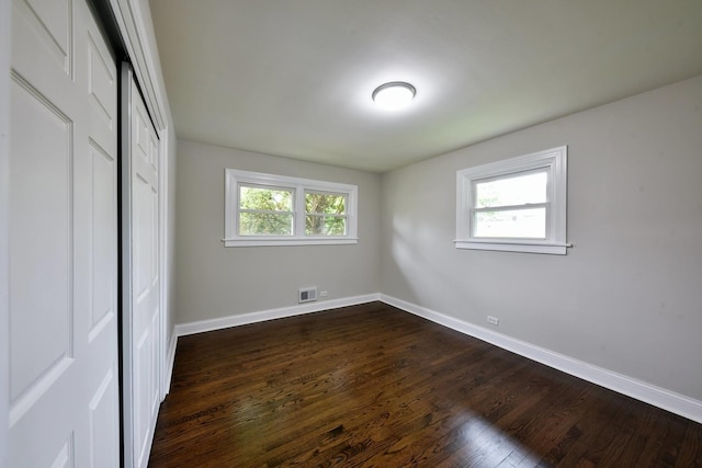 unfurnished bedroom with multiple windows, dark wood-type flooring, and a closet