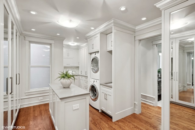 laundry room featuring ornamental molding, stacked washer / drying machine, cabinets, and wood-type flooring