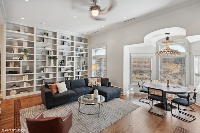 living room featuring hardwood / wood-style floors, built in features, ornamental molding, and ceiling fan